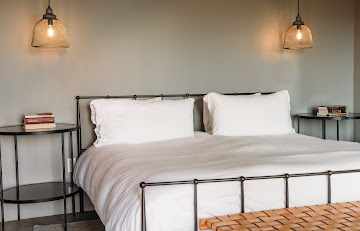 A neatly made bed with white bedding and pillows, flanked by two small side tables and pendant lights hanging above.