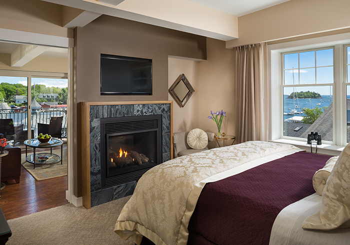 A bedroom with a fireplace, balcony, and water view.
