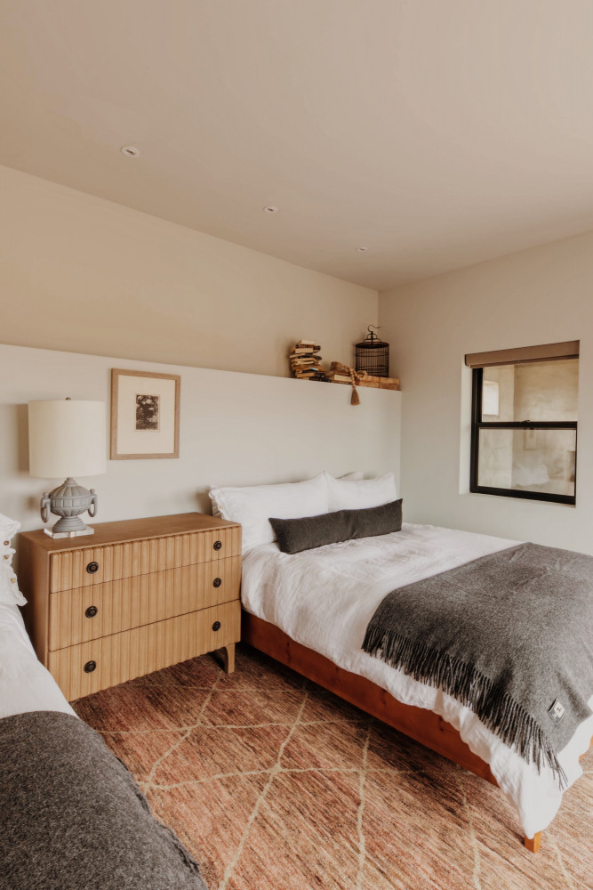 A hotel room with two beds, a wooden dresser, a window, and a shelf with decorative items.