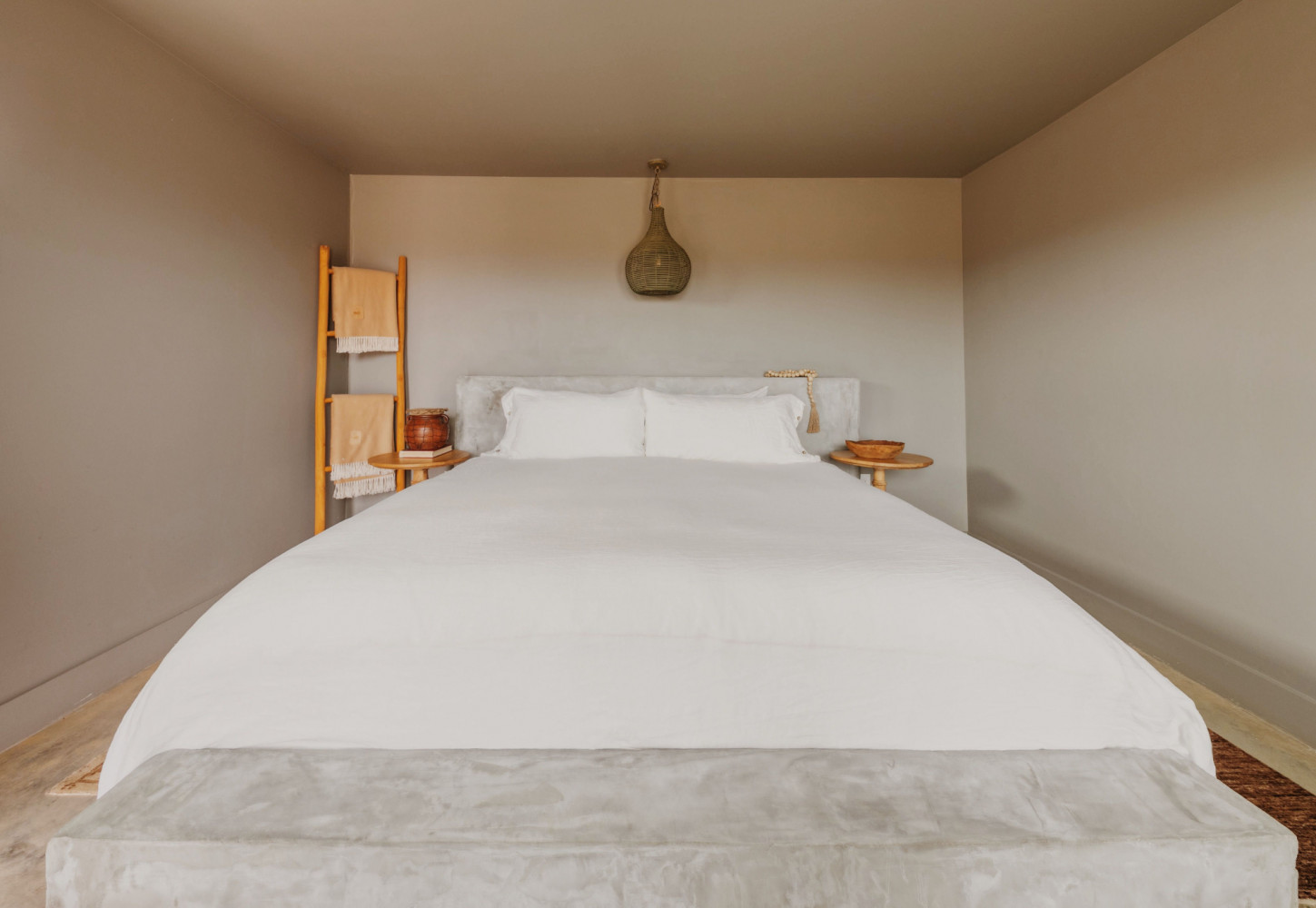 A neatly made bed with white linens and pillows, flanked by two small wooden nightstands with lamps and towels on a ladder to the left.