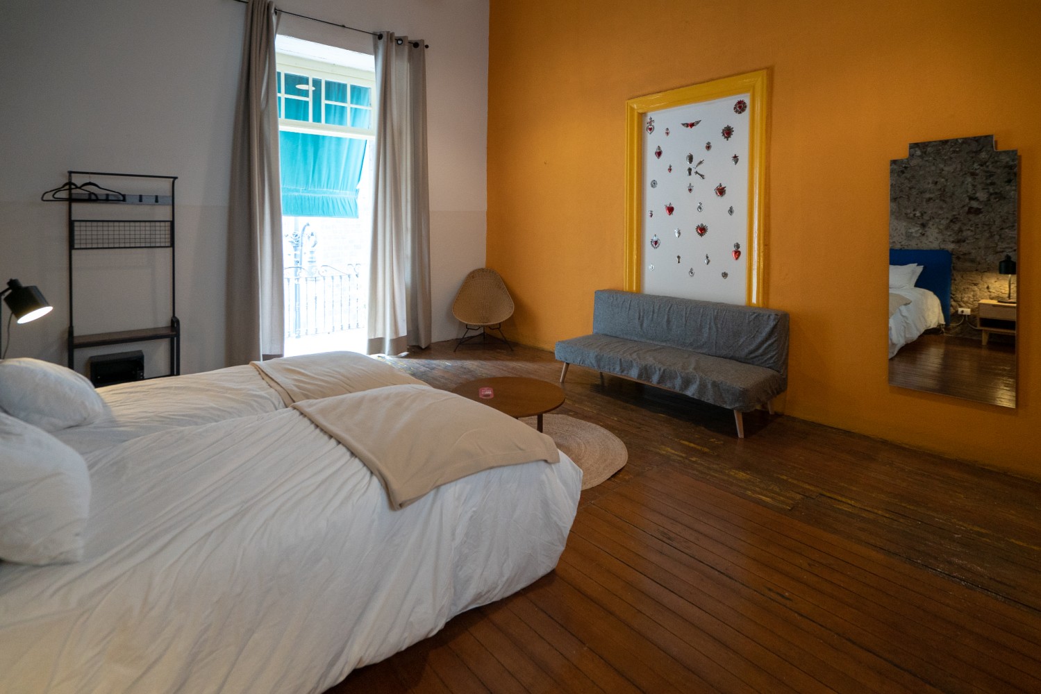 A wide view of a room with a bed, sofa, mirror, and window.
