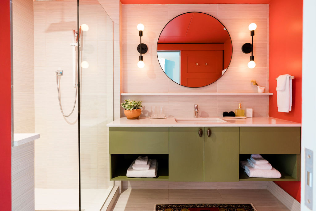 A modern bathroom with green cabinets, red walls, and a round mirror