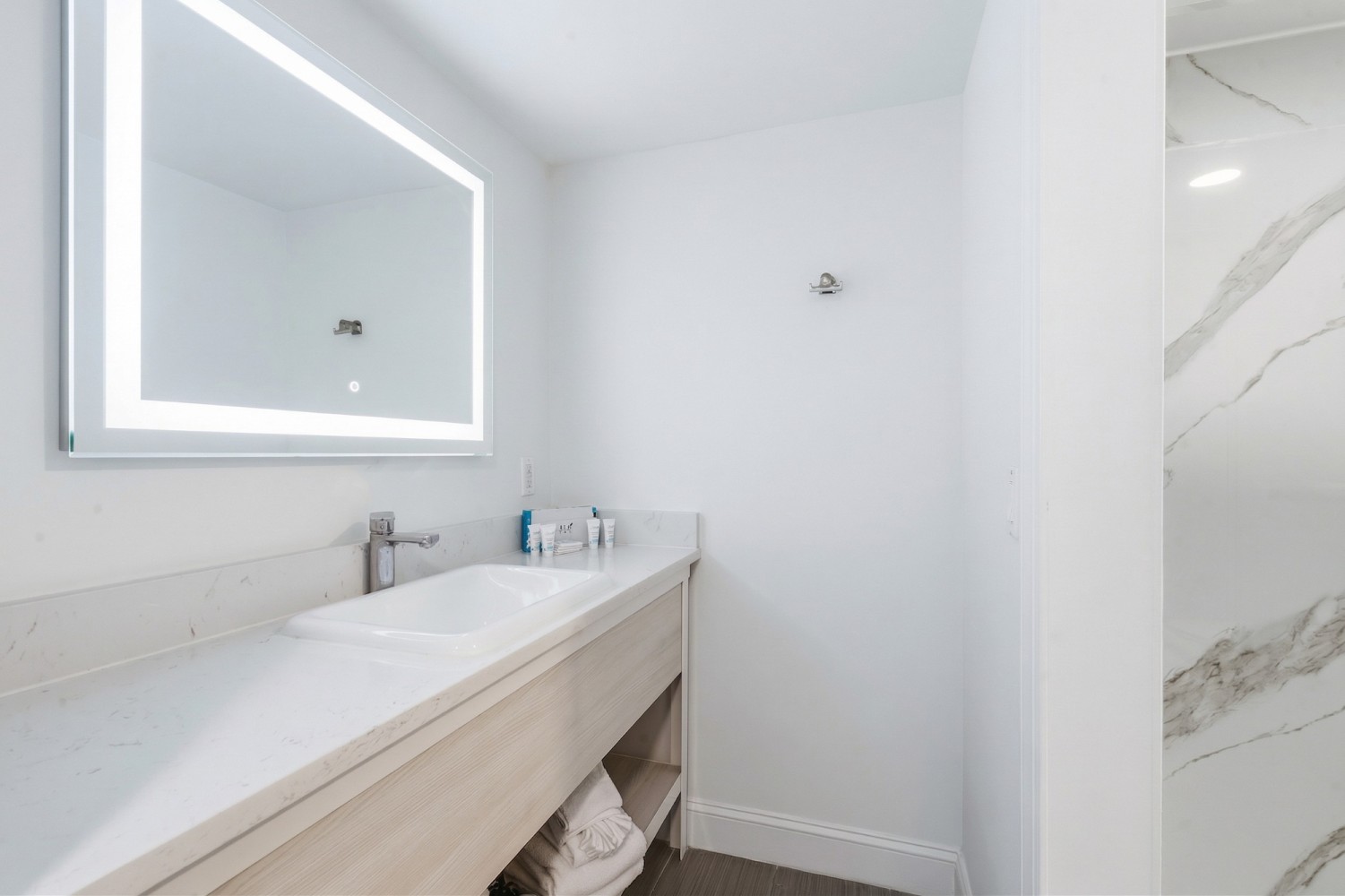 A modern bathroom sink with a large mirror, marble countertop, and toiletries.