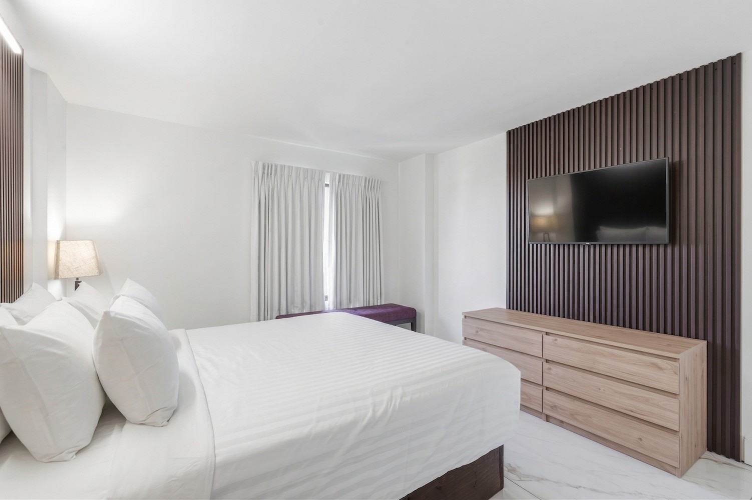 A hotel room with a large bed, wooden dresser, and flat screen TV mounted on a slatted wood wall.