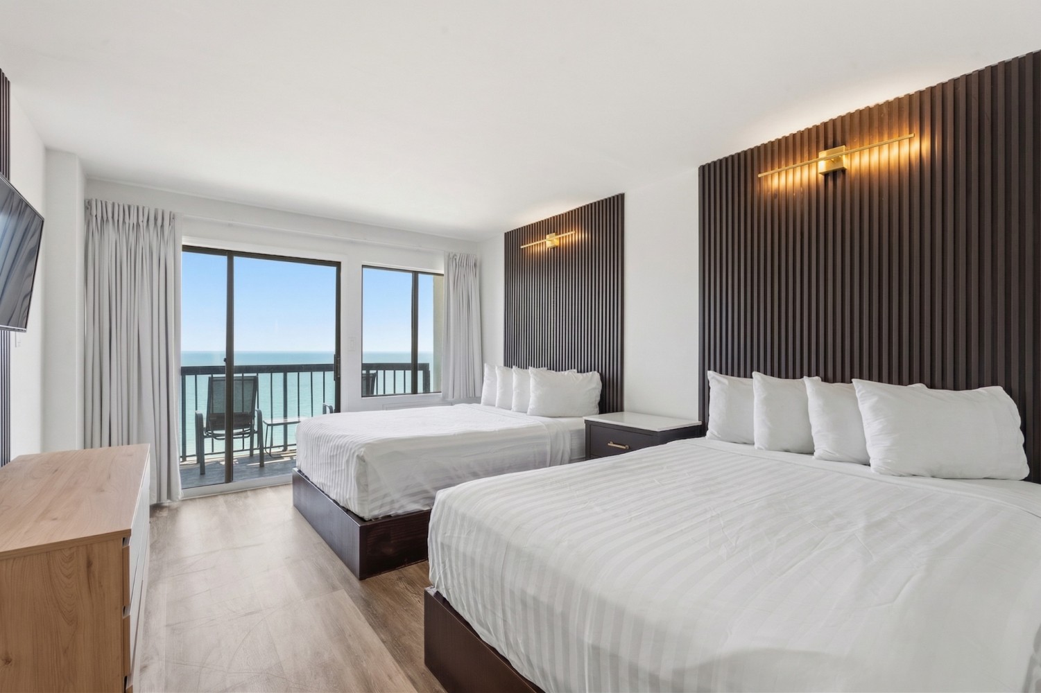 A modern hotel room with two double beds, a balcony, and an ocean view.