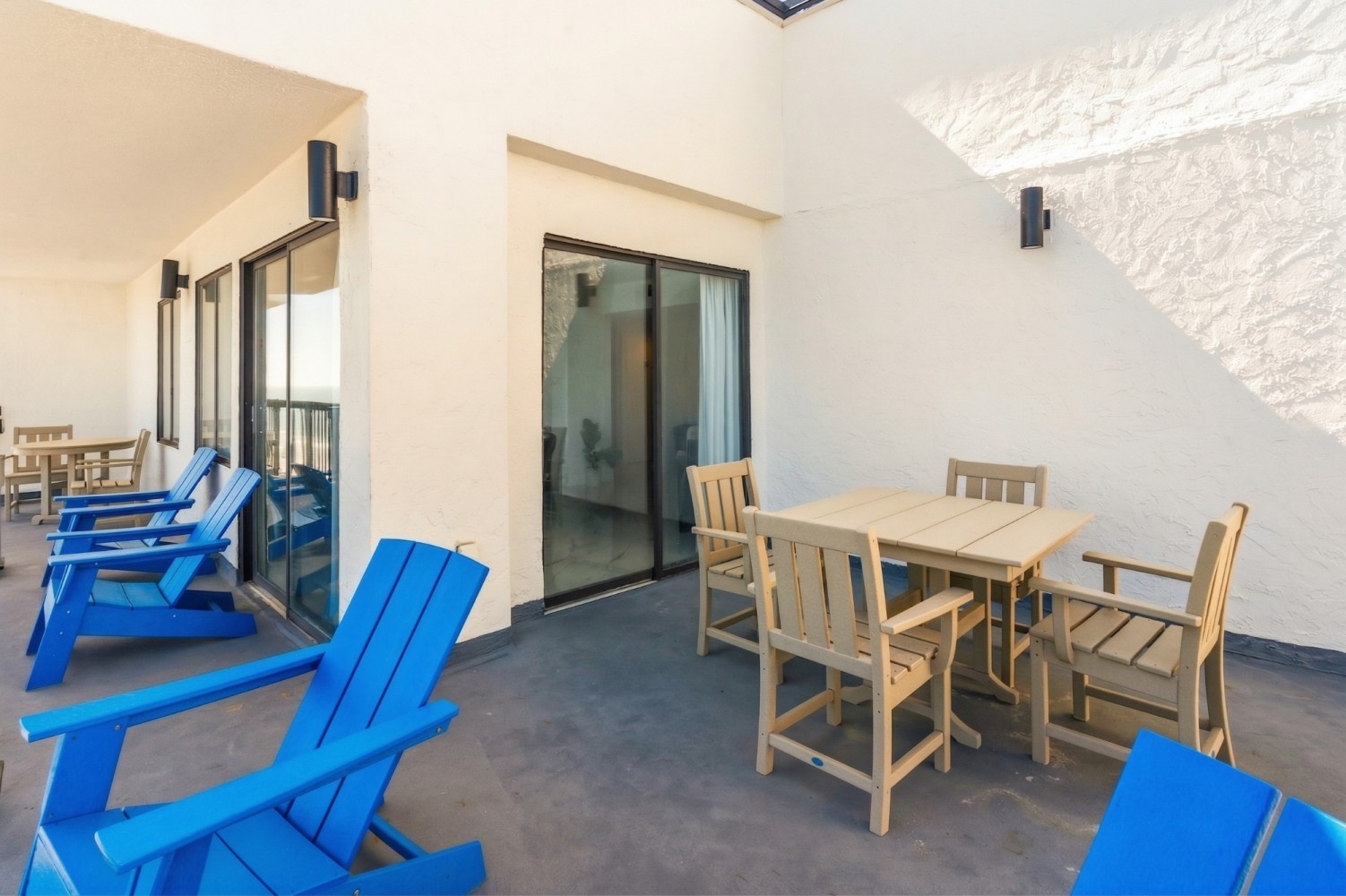 A patio area with outdoor furniture, including blue Adirondack chairs and a wooden table with chairs.