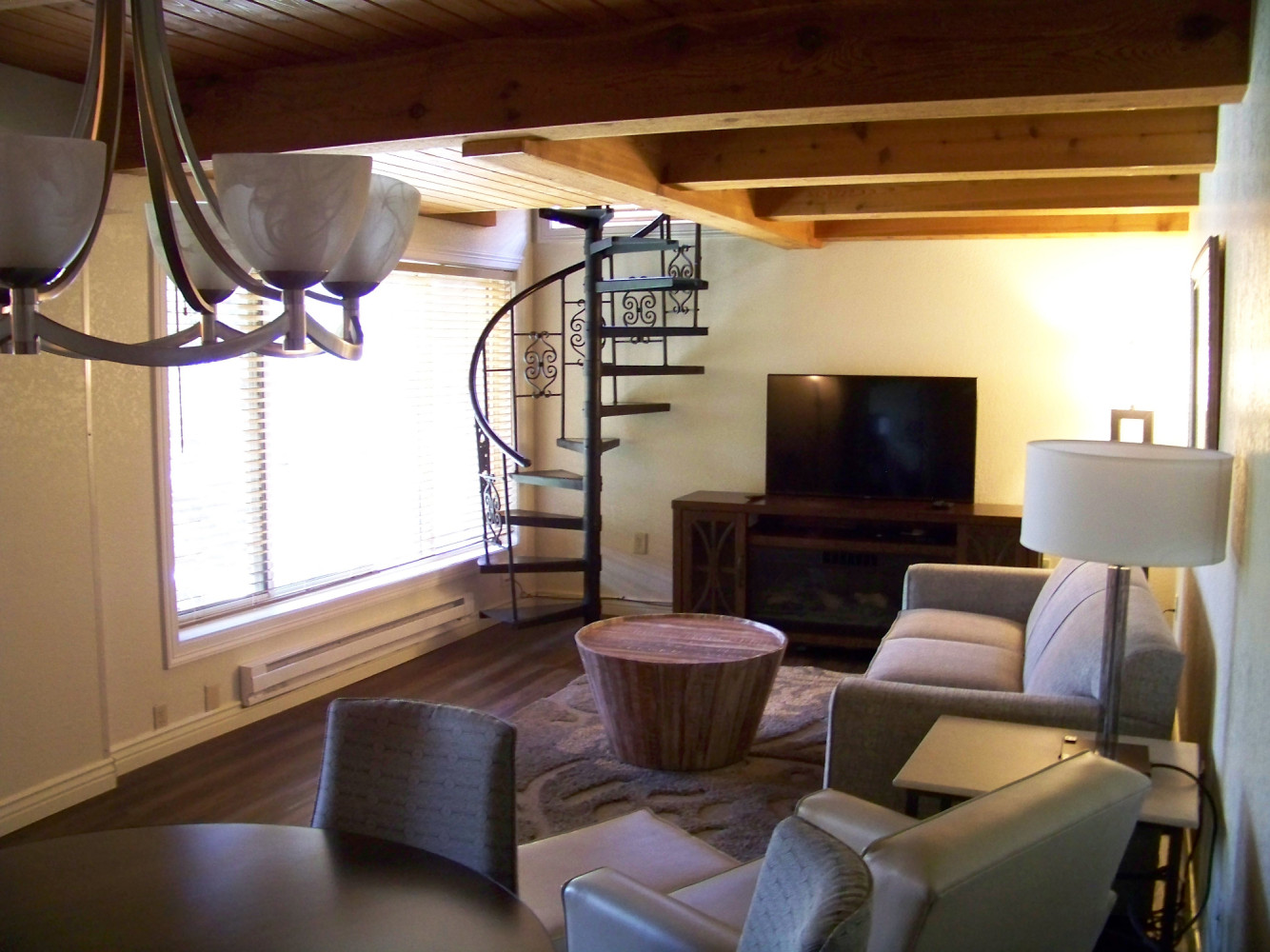 A living room with a spiral staircase, wood beam ceiling, and modern furniture