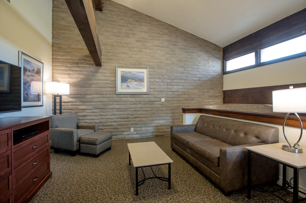 A hotel living room with a sofa, chair, coffee table, TV, and lamp