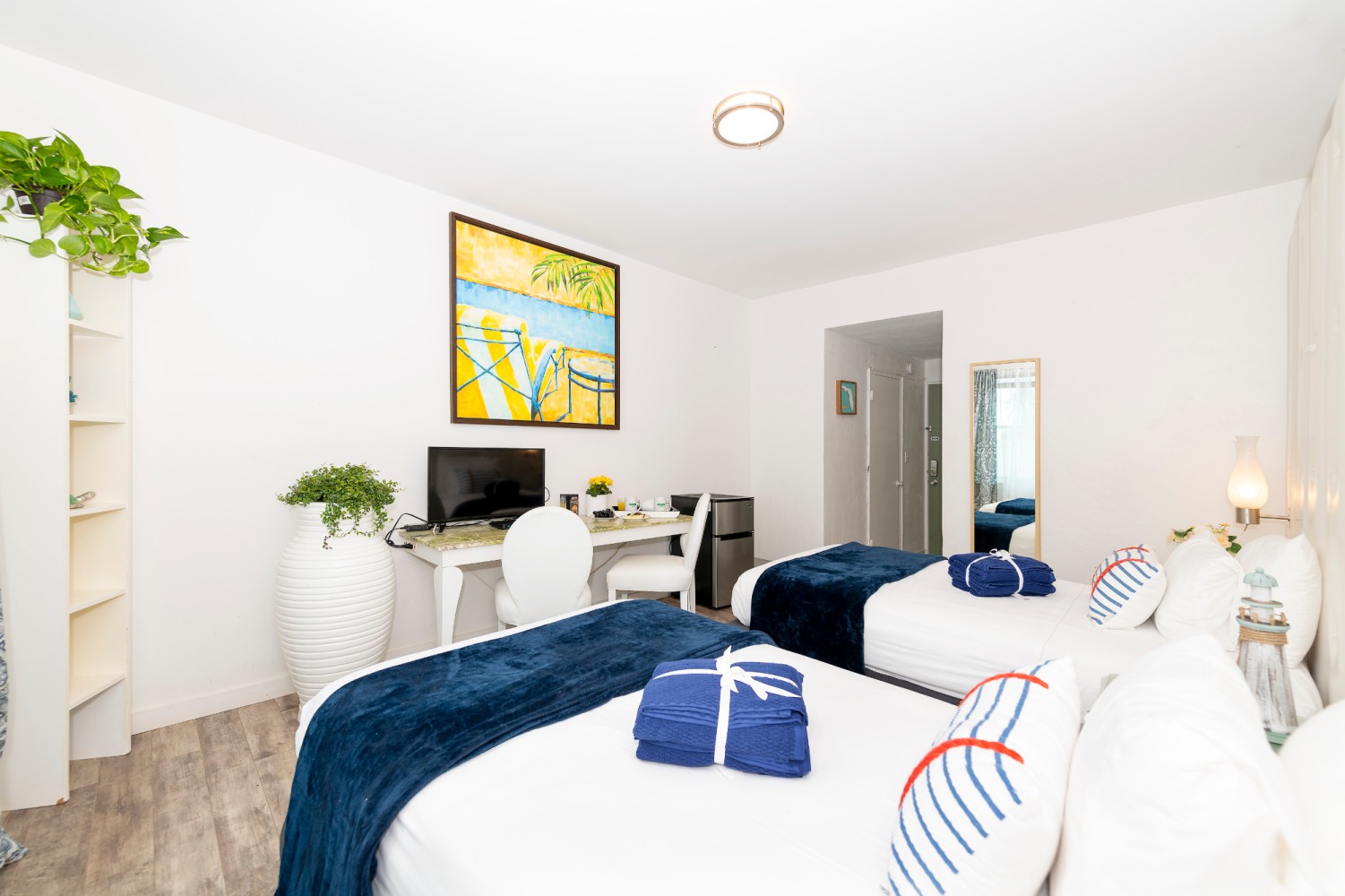 A hotel room with two twin beds, a desk, TV, and mirror.