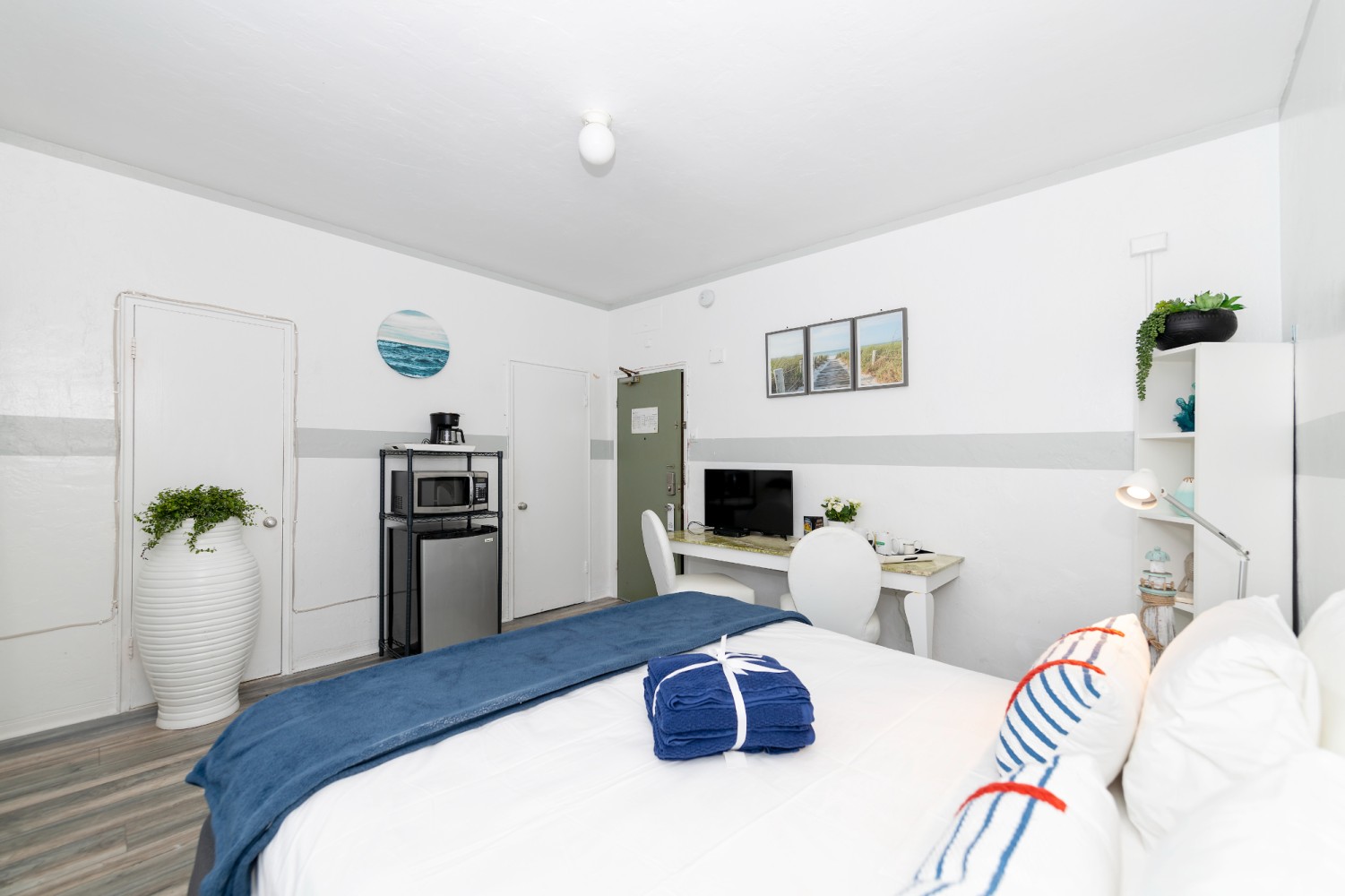 A tidy hotel room with a bed, desk, mini-fridge, and TV.