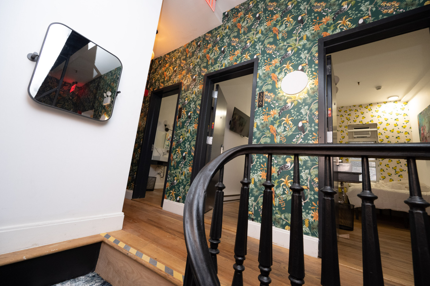 A staircase with a black railing and floral wallpaper leading to a room with a bed