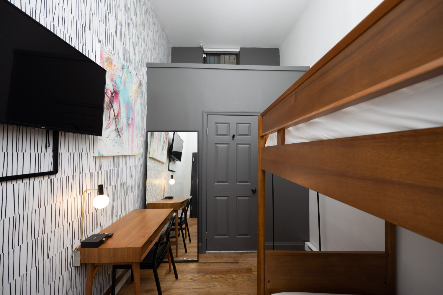 A room with a bunk bed, desk, TV, and abstract art