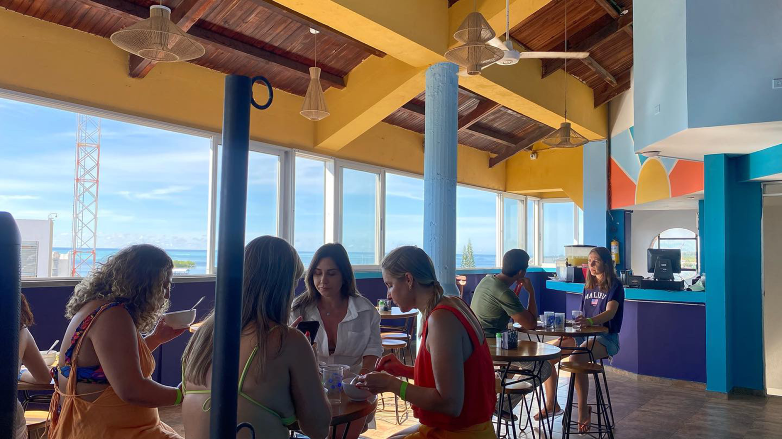 a group of people sitting at tables in a colorful dining area with a view of the ocean